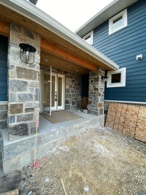 Stone entryway with porch, open double doors, and blue siding. Under construction.