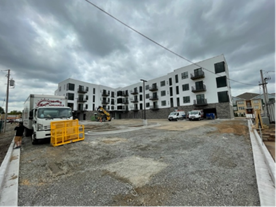 Multi-story white building under construction with truck, vehicles, and construction equipment.