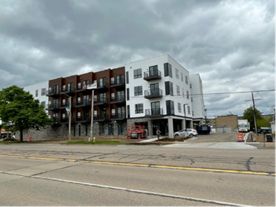 Multi-story apartment building with white and brown facade, under cloudy skies. Construction visible.