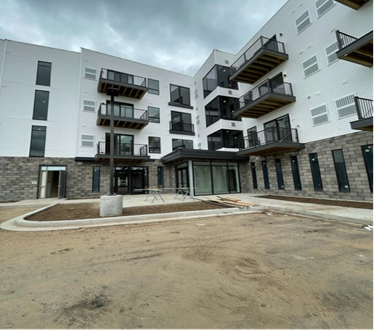 Modern multi-story building with balconies, gray and white exterior. Entryway with glass doors.