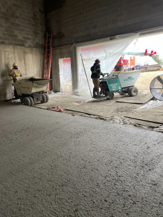 Construction workers smoothing concrete floor in a building using motorized wheelbarrows.