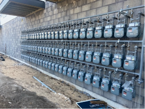 Rows of gas meters mounted on a gray brick wall.