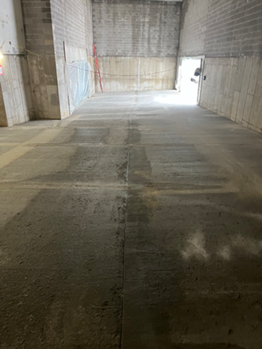 Concrete floor and walls in a building under construction, with a doorway at the far end.