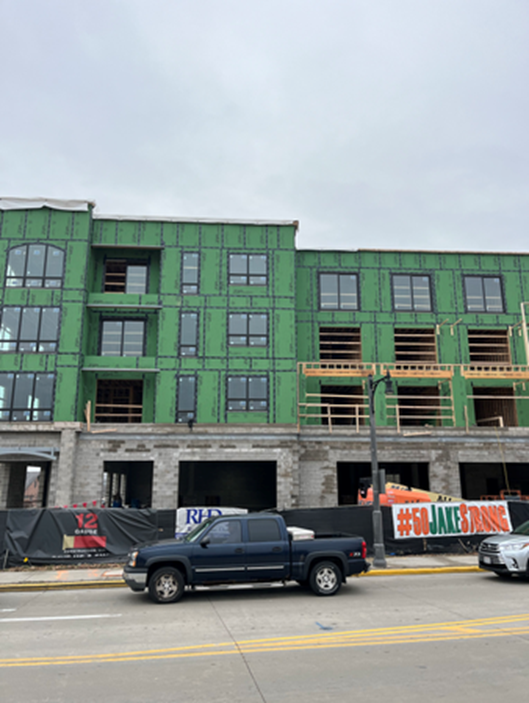 Building under construction with green sheathing, windows, and scaffolding; a truck is in front.
