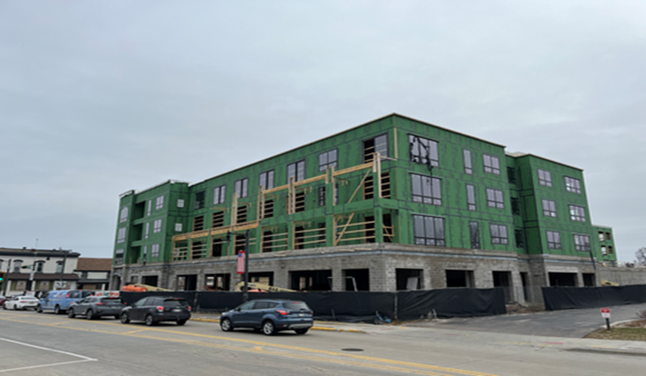 Multi-story building under construction with green exterior, windows, and parked cars on the street.