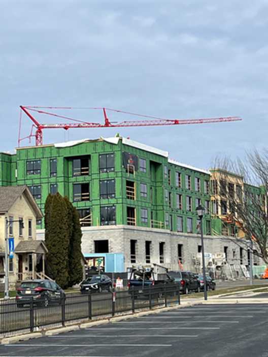 Construction site with a red crane and multi-story building frame wrapped in green.
