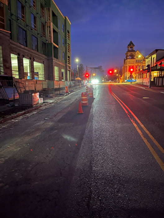 Street view at dusk with construction on the left and a building with a clock tower in the distance.
