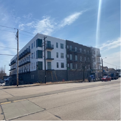Multi-story apartment building under construction, exterior view. White and brown sections, balconies, blue sky.