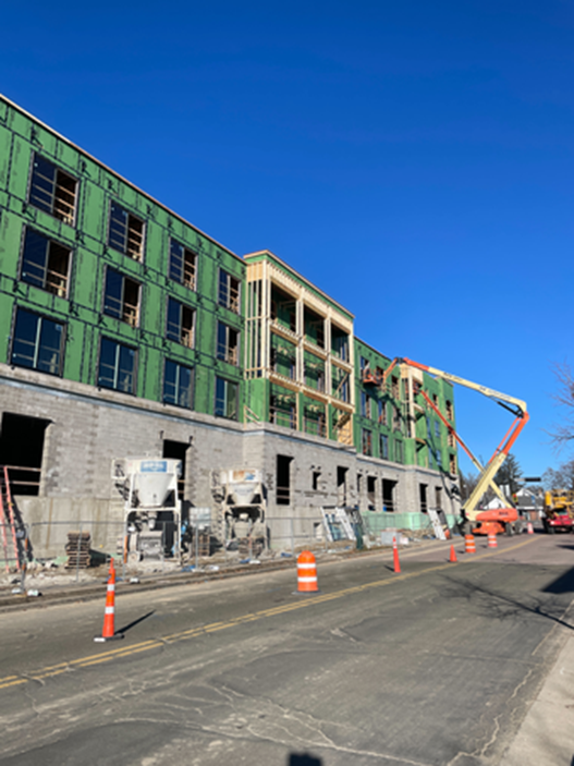 Building under construction with green insulation, stone facade, and a boom lift on a sunny day.