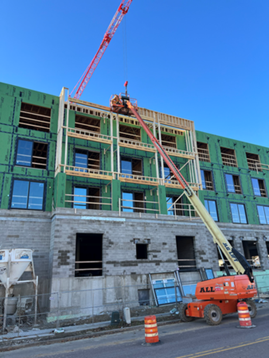 Building under construction with a crane and lift. Workers are on the upper floors, clear sky, street view.