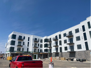 A red pickup truck in front of a white apartment building under construction on a sunny day.