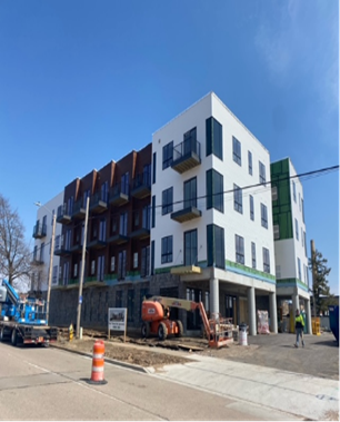 Multi-story apartment building under construction, blue sky. Scaffolding, crane, and construction equipment present.