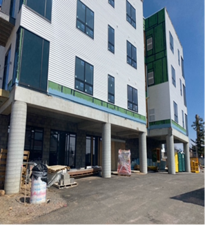 Multi-story building under construction with white siding, columns, and blue sky.