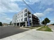 Modern multi-story apartment building with balconies, sidewalk, and street. Blue sky with clouds.