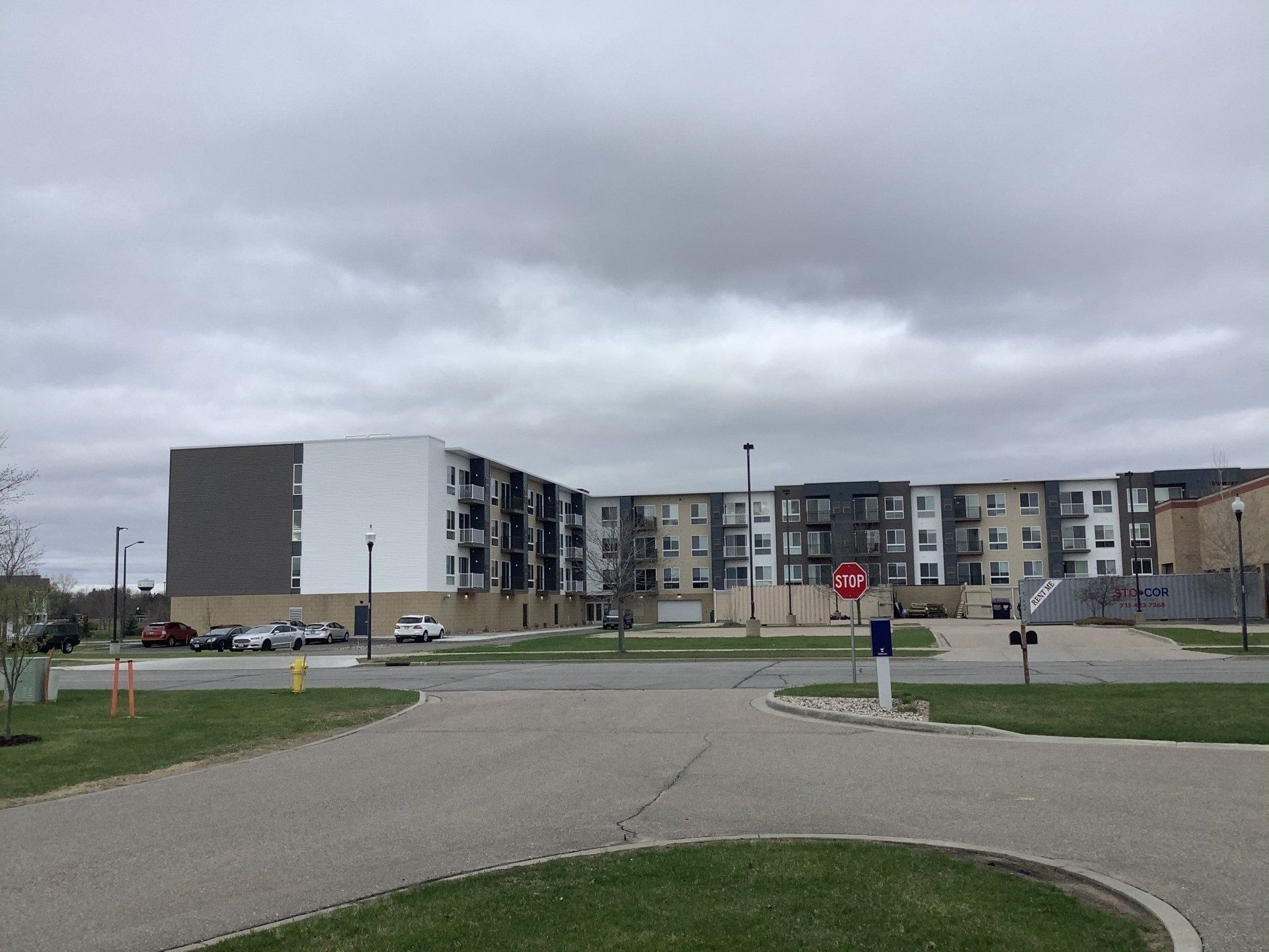 Multi-story apartment building under overcast sky, with a parking area in the foreground.