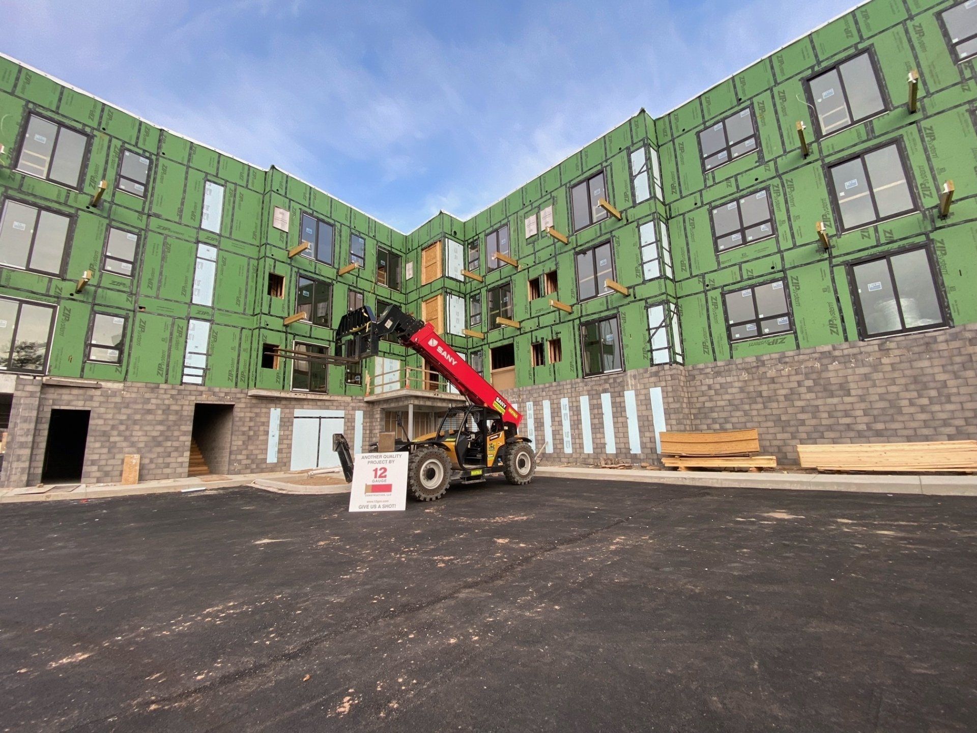 Construction site with a red telescopic handler in front of a green-sheathed building, and a gray stone wall base.