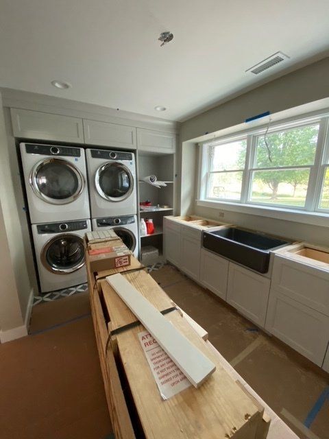 Laundry room with stacked washer/dryer, cabinetry, window with a sink, and construction materials.
