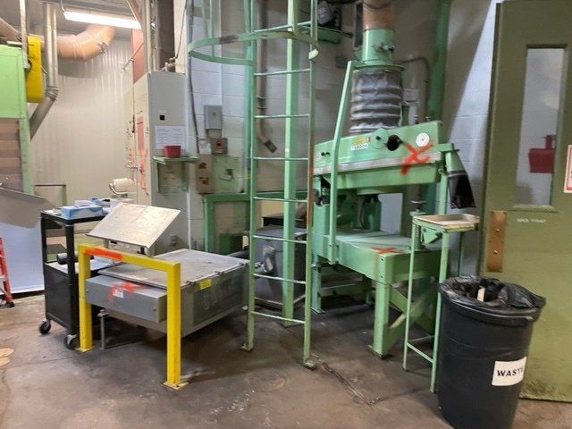 Industrial machines in a factory setting; green, gray, and yellow equipment with a black trash can.