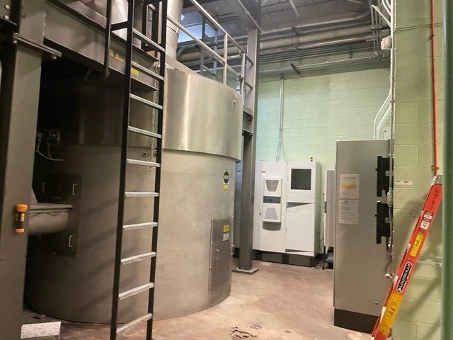 Industrial room with cylindrical metal tanks, machinery, and electrical panels. A ladder is present.