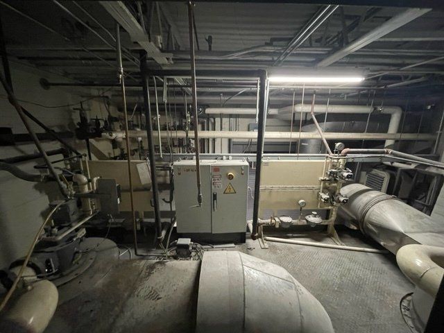 Industrial equipment in a dimly lit room with pipes, a control box, and ductwork.
