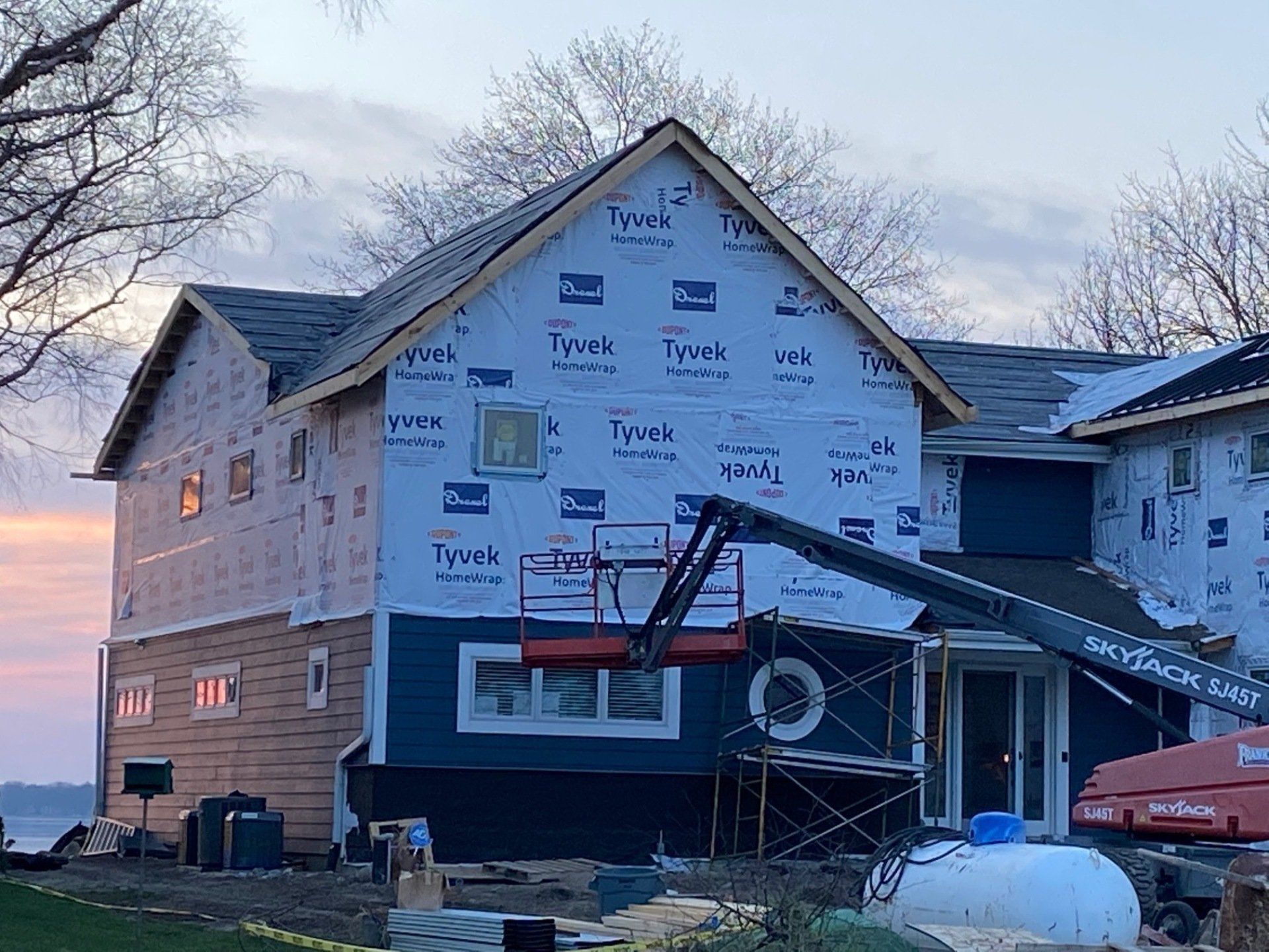 House under construction with blue siding and Tyvek wrap. A lift is present.