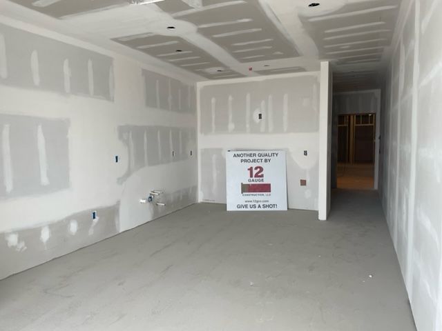 Interior room under construction, with drywall on walls and ceiling, concrete floor. Sign in the center.