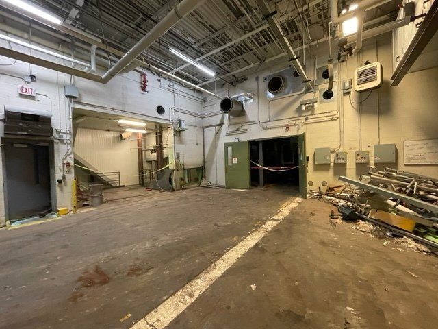 An industrial room with concrete floor, pipes, and open doorways, likely a utility area, interior view.
