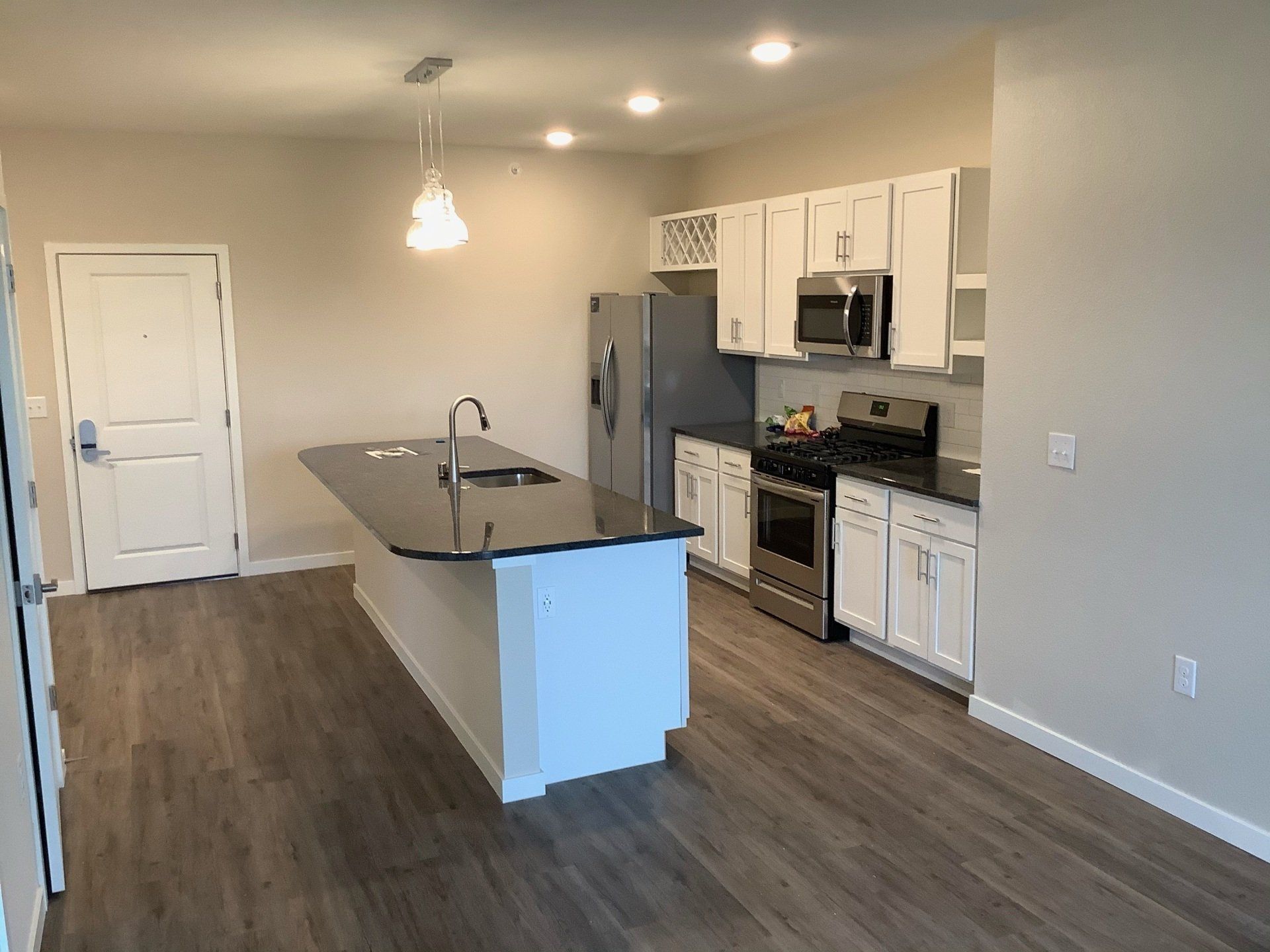 Kitchen with white cabinets, stainless steel appliances, dark countertop island, and wood-look flooring.