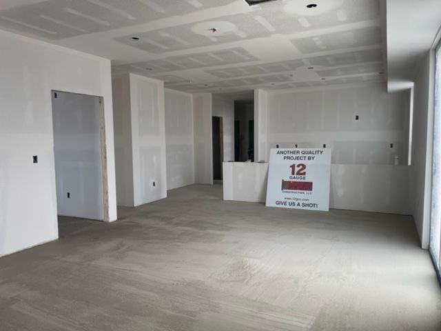 Interior room under construction, drywall on walls and ceiling, bare concrete floor.