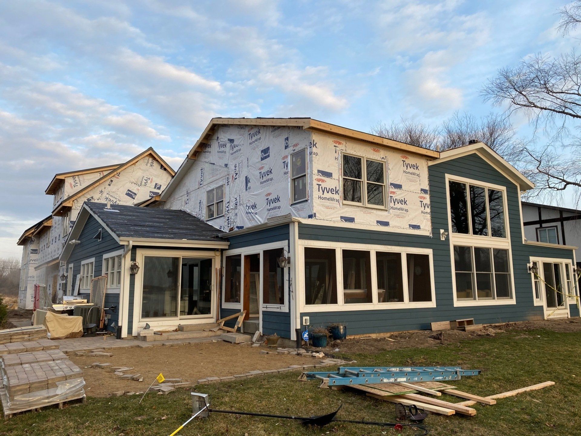 House under construction, blue siding, windows, and tarpaper visible.