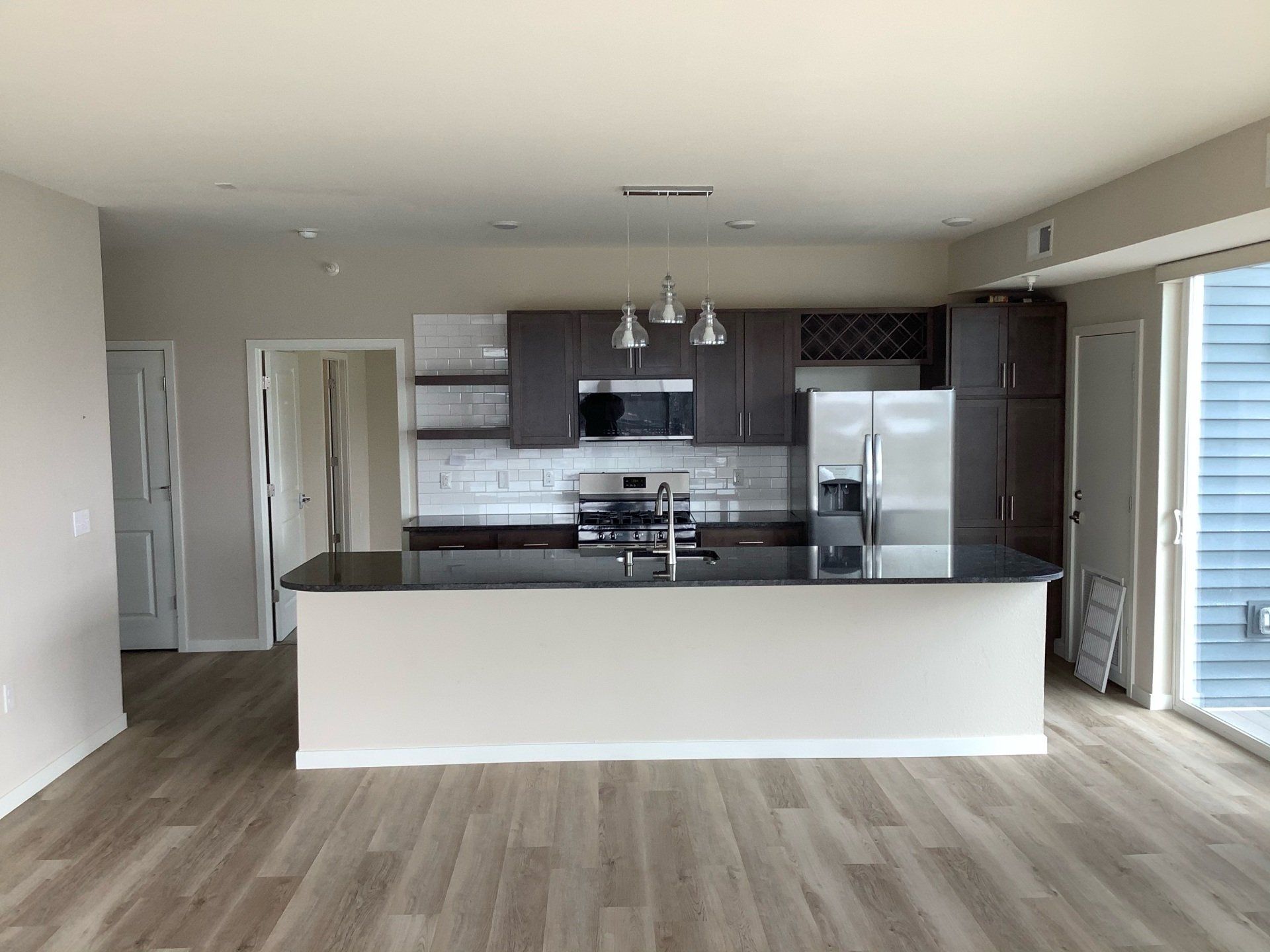 Open-concept kitchen with an island, stainless steel appliances, dark wood cabinets, and light wood flooring.
