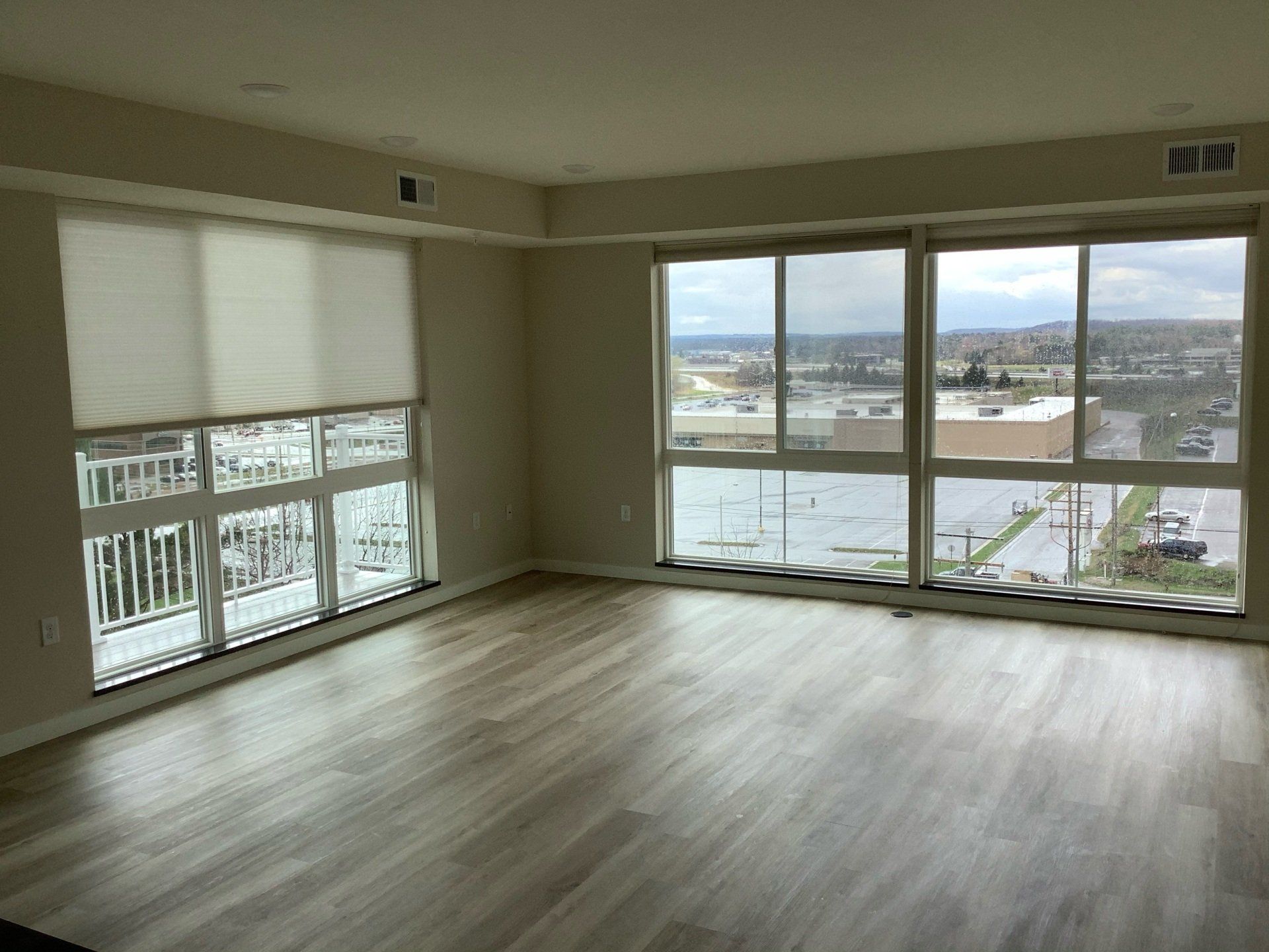 Empty living room with large windows, city view, and wood-look flooring.