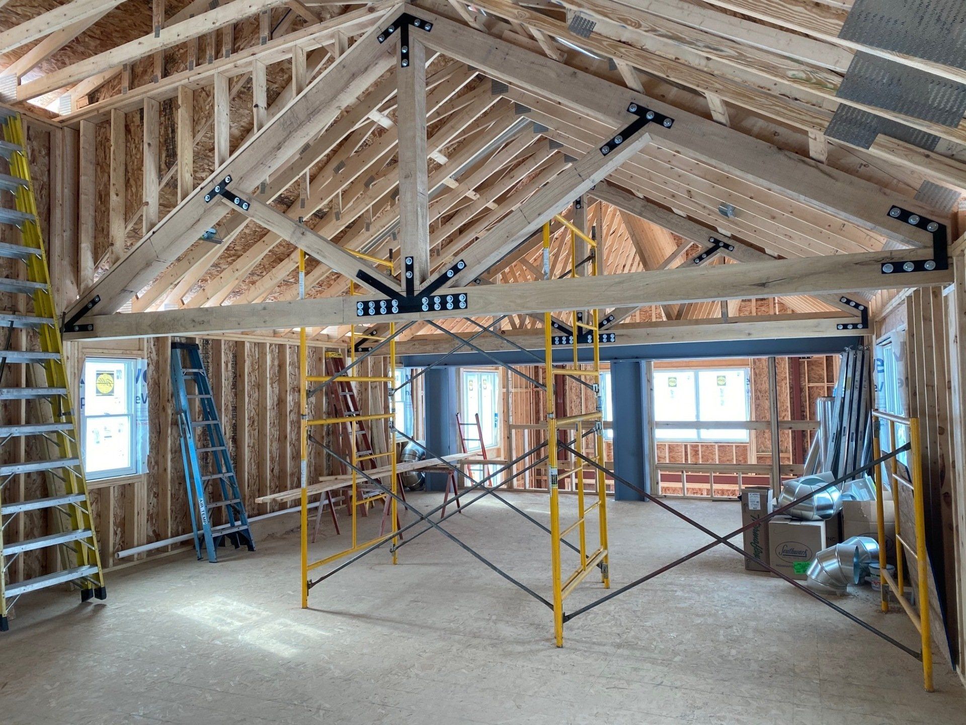 Interior view of a building under construction, showing wooden framing, roof trusses, and scaffolding.