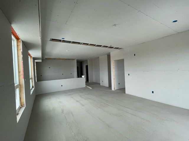 Interior of a room under construction, with drywall walls and ceiling, window frames, and open doorways.