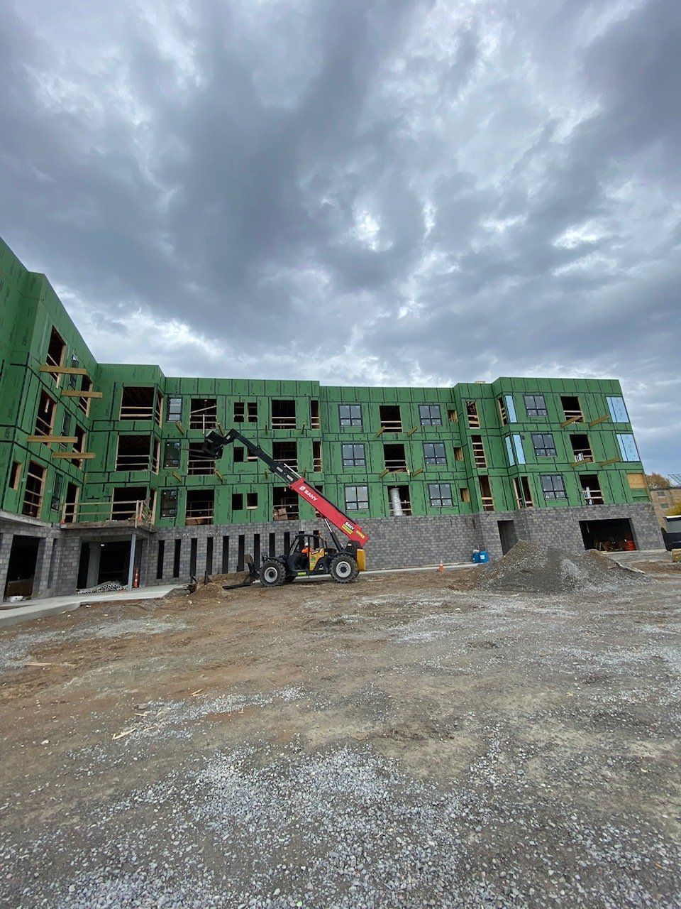 Construction site with unfinished multi-story building under a cloudy sky. A forklift operates on the ground.