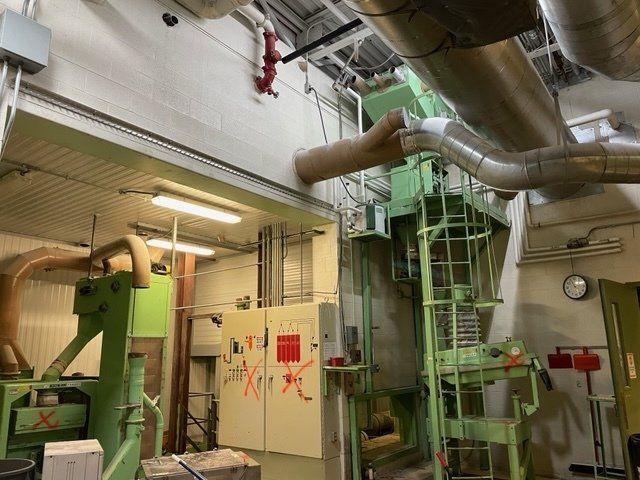 Industrial interior: large green machinery, metal pipes, control panel, and an overhead walkway.