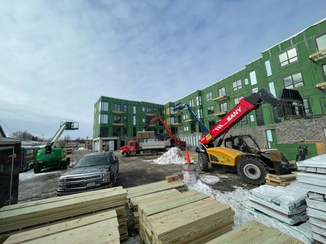 Construction site with a multi-story building under construction; heavy machinery, lumber, and a truck are present.