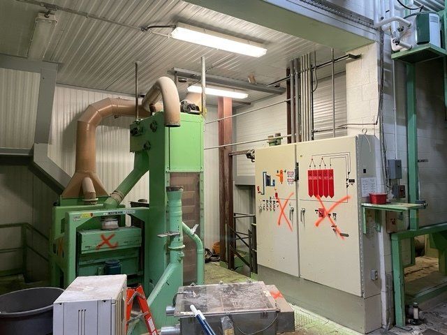 Industrial equipment in a factory setting; green machinery with ductwork, electrical panel with red markings, and a white ceiling.