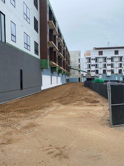 Construction site with buildings and dirt path. Fenced area with construction equipment visible.