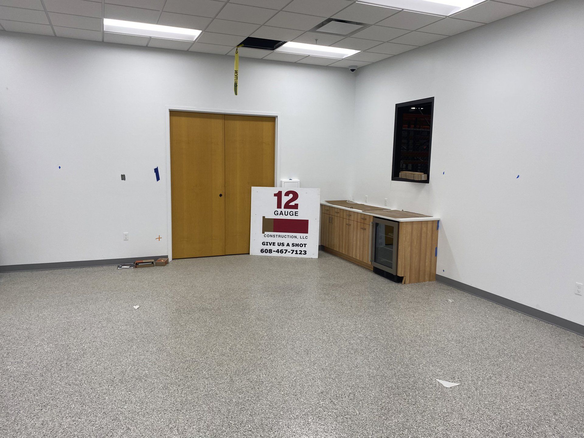 Empty room with light-colored walls, speckled floor, a closed wooden door, and a cabinet with a small window.
