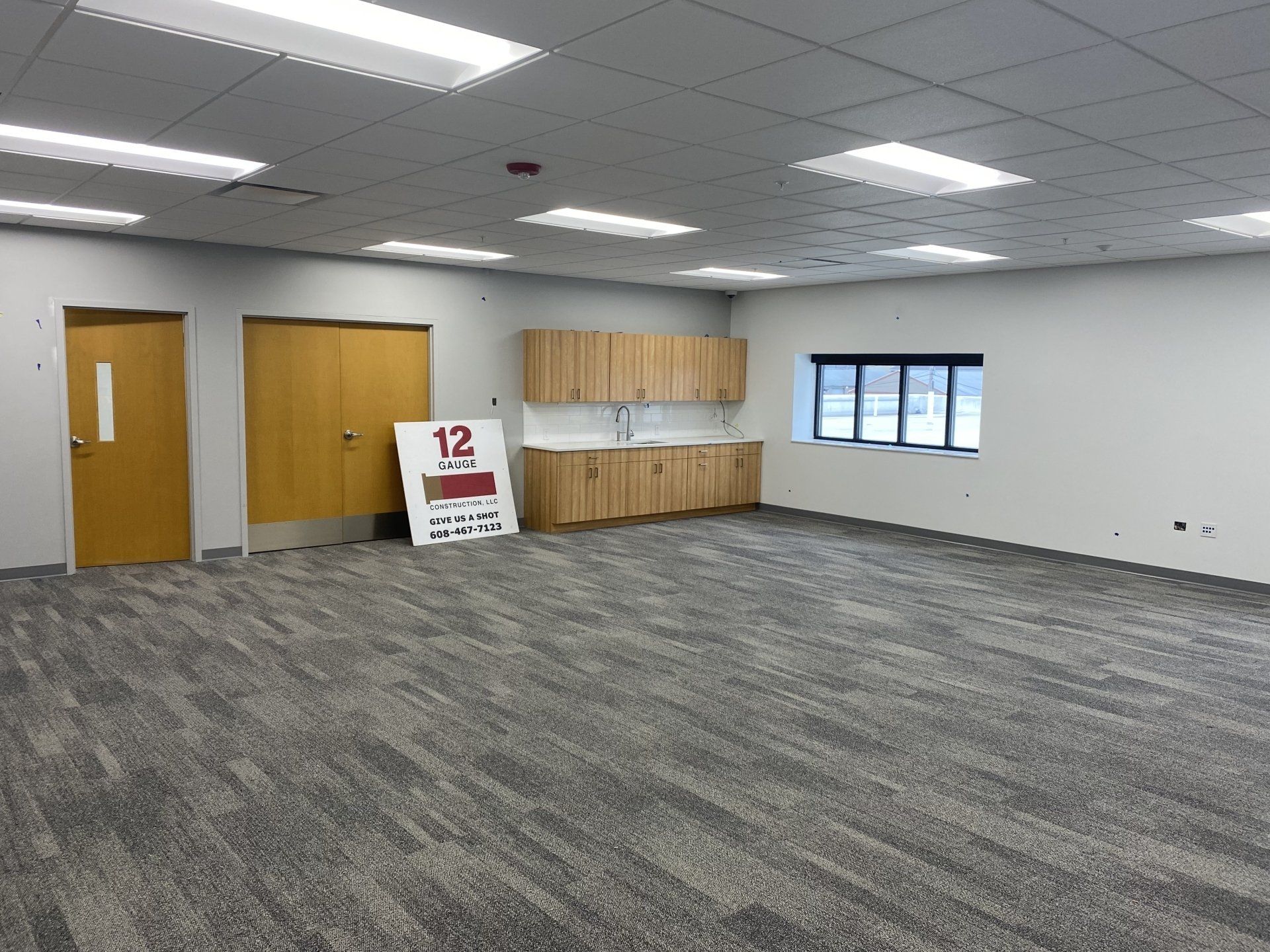 Empty room with cabinets, two doors, a window, and gray carpet.