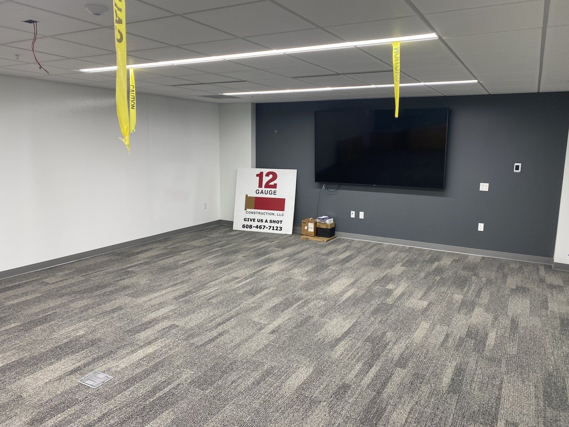 Empty room with gray carpet, white and gray walls, a large TV, and caution tape.