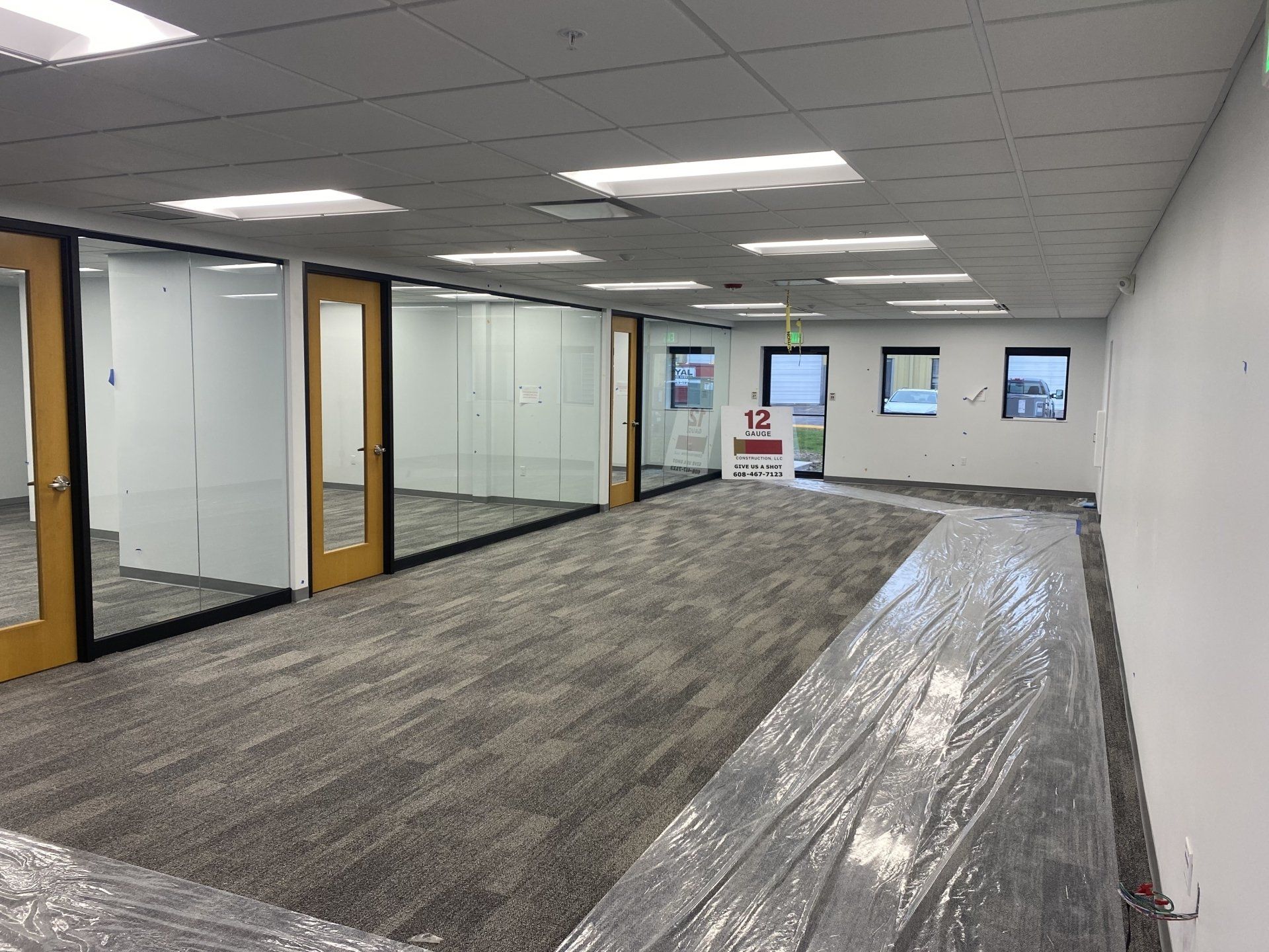 Empty office space with carpet, glass-walled rooms, and white walls. Packaging lies in the foreground.