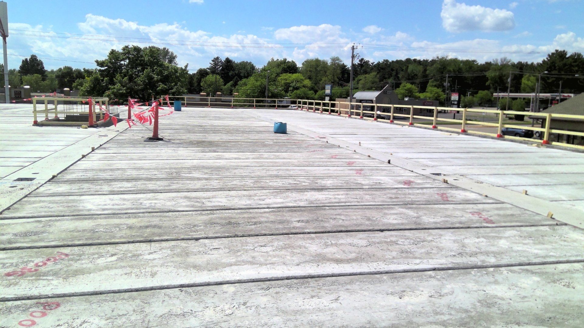 Concrete slab, possibly a roof or parking deck, with safety barriers and trees in background.