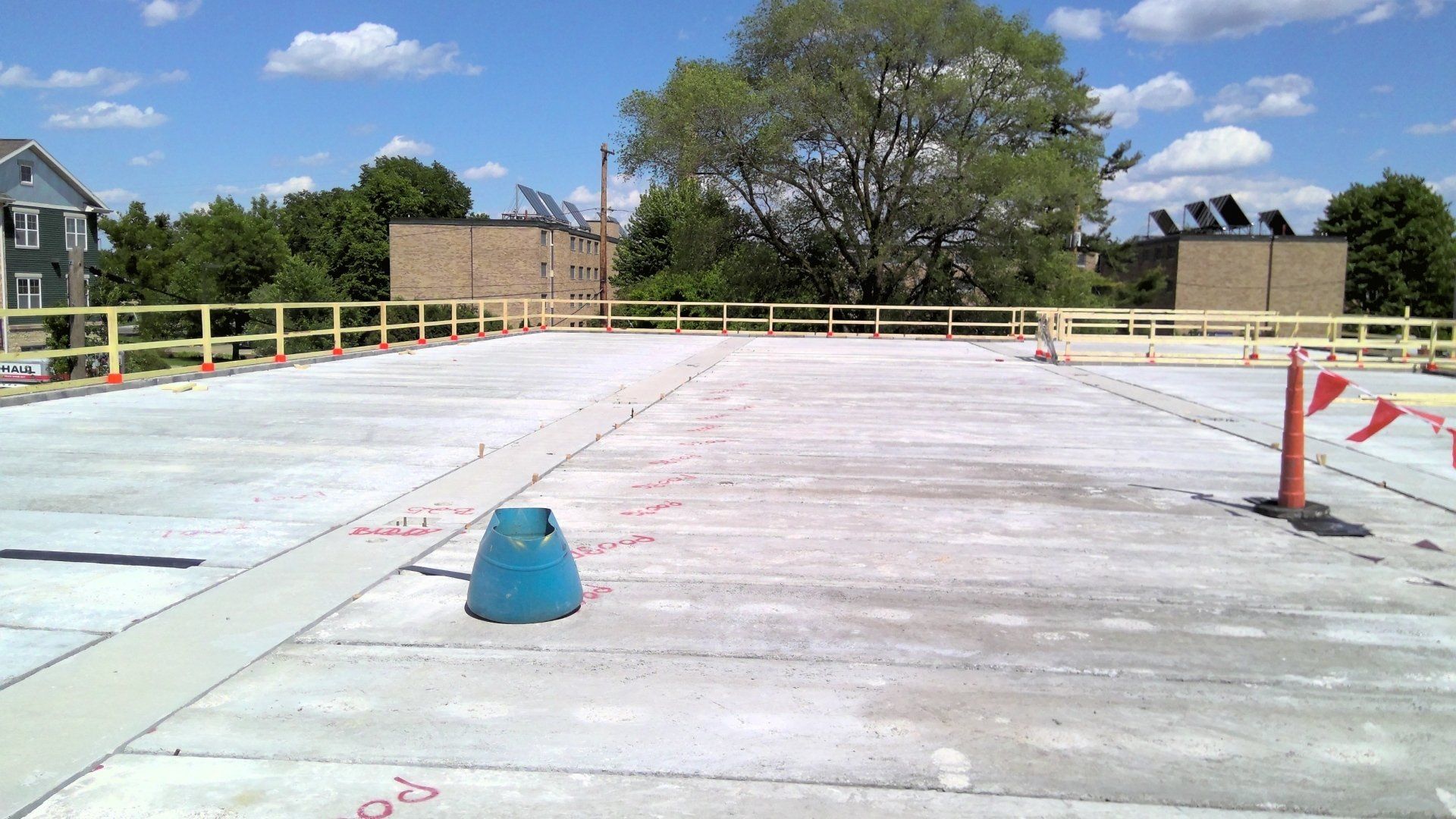Construction site with concrete surface, safety railings, and orange cones under a blue sky.