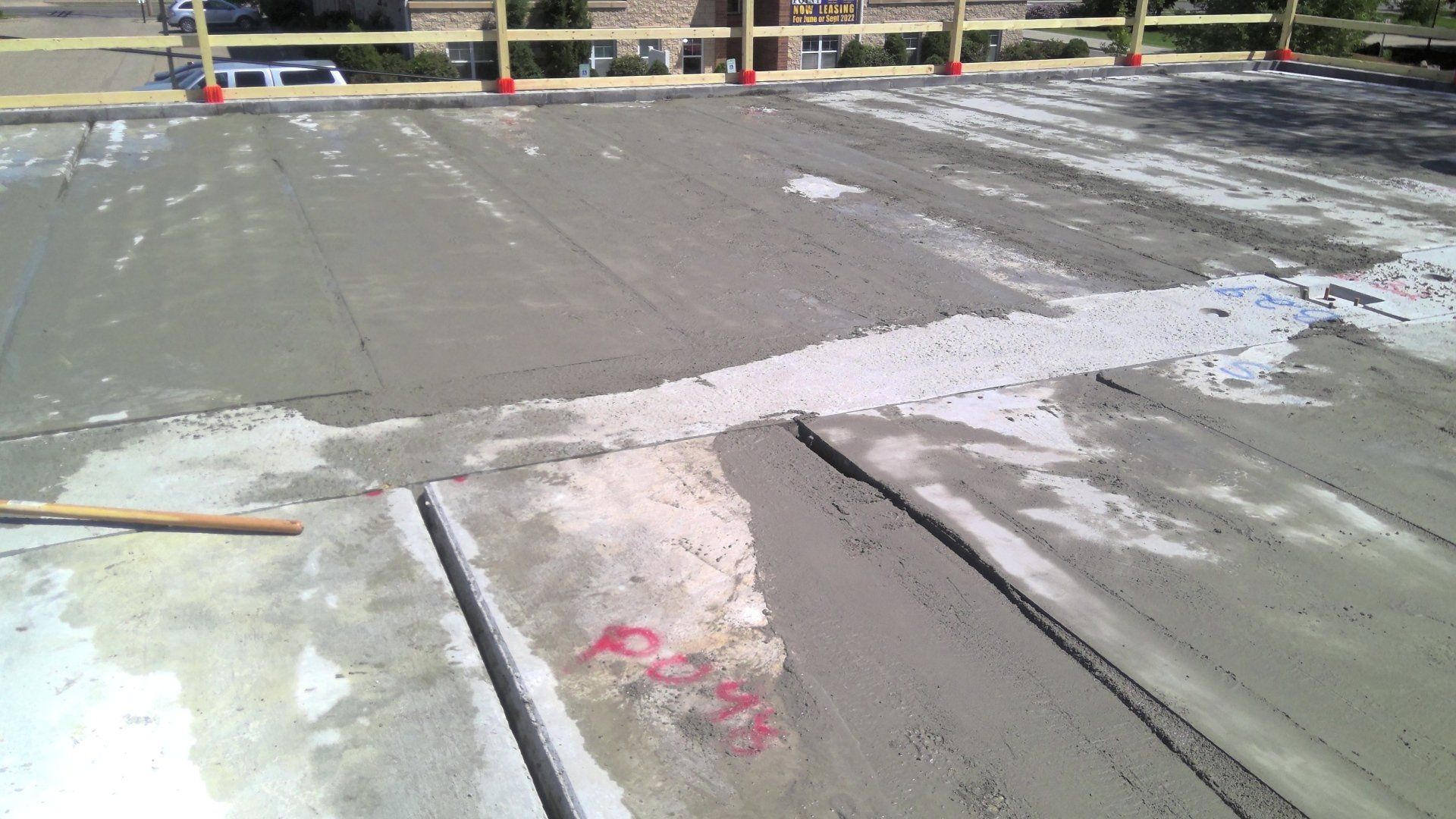 Fresh concrete being poured onto a construction site floor, with a wooden barrier in the background.