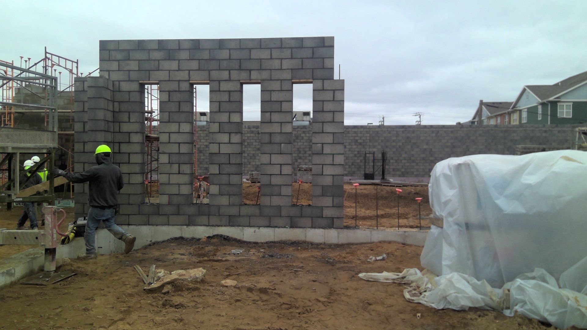 Construction worker building a cinder block wall at a construction site on an overcast day.