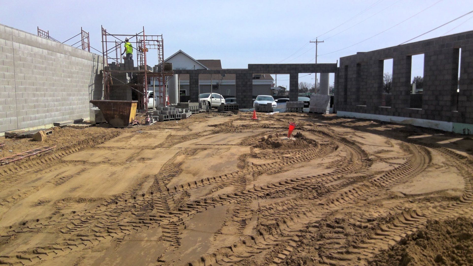 Construction site with block walls, dirt ground with tire tracks, and workers on scaffolding.