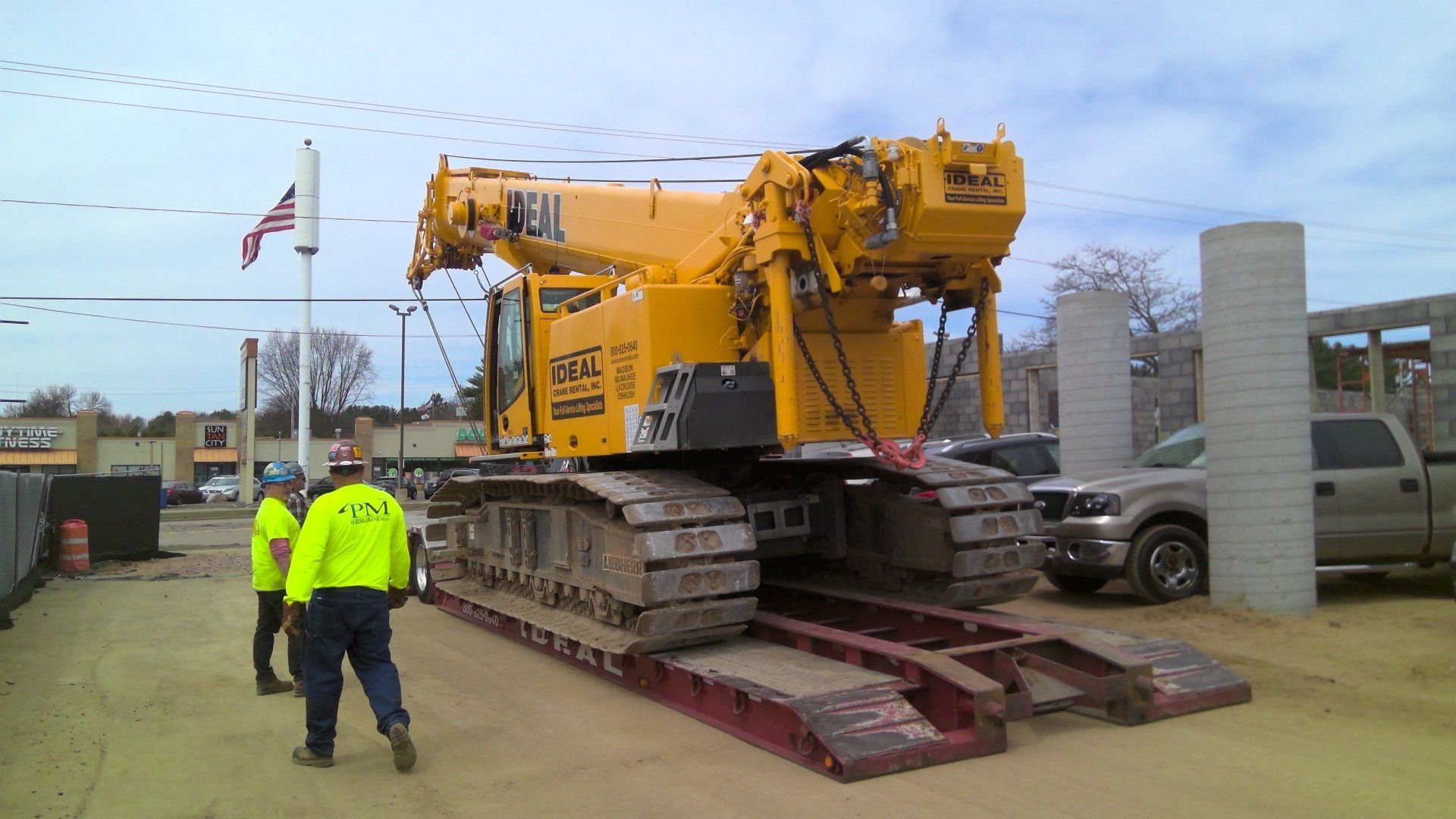 Yellow crane on a trailer at a construction site with two workers in safety vests.