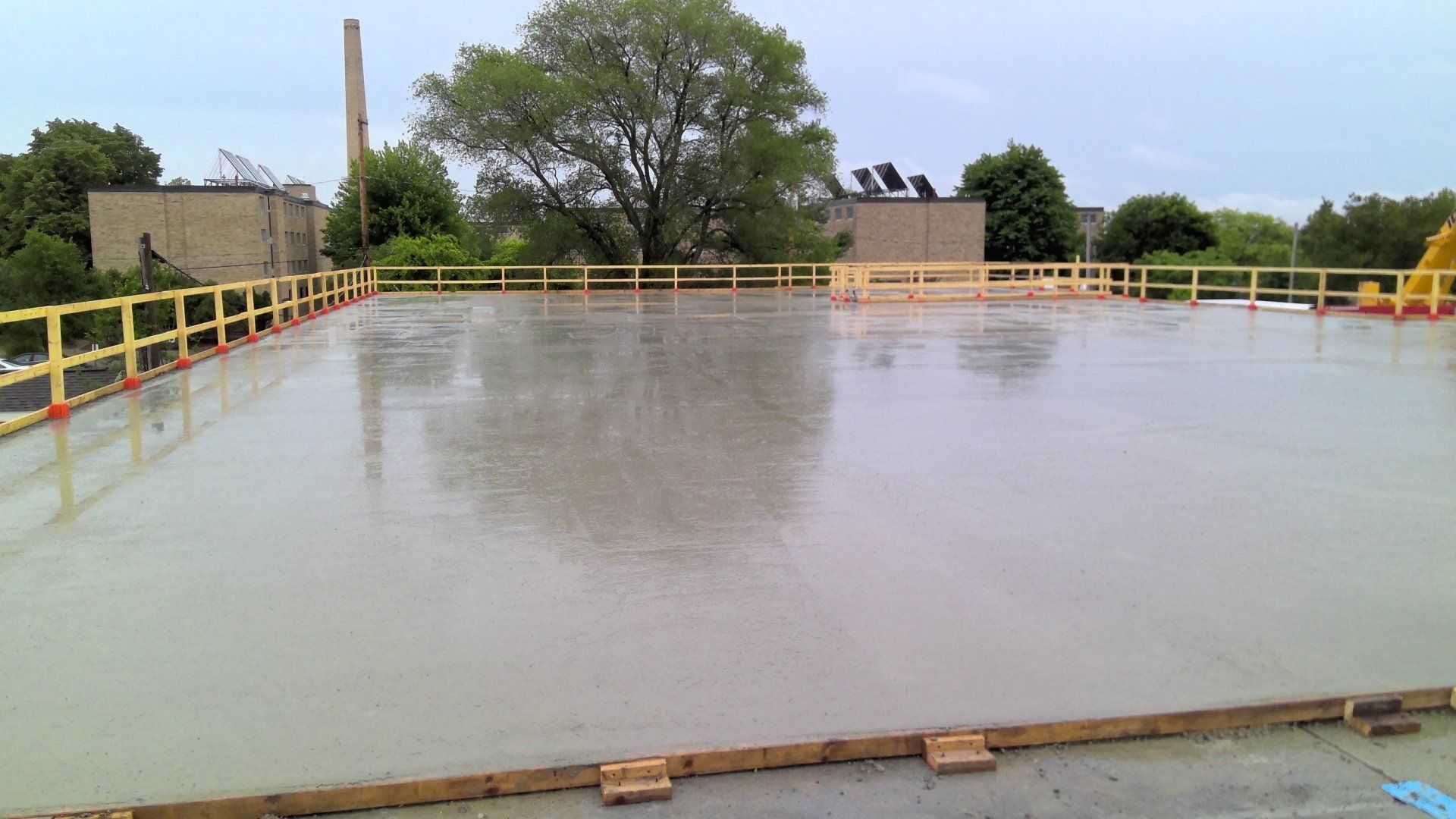 Newly poured concrete flatwork on a rooftop, surrounded by yellow and wooden safety railings.